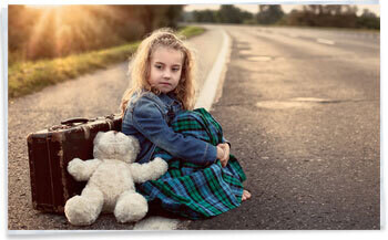 Young girl sitting beside the road with suitcase and teddy waiting